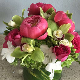 Pink peonies, roses, and white orchids in a green glass vase
