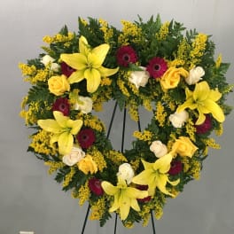 Heart-shaped floral wreath with yellow lilies, roses, and burgundy gerberas