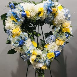 Heart-shaped floral wreath with blue, white, and yellow flowers on a stand