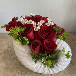 Red roses and white filler flowers in a white ceramic vase