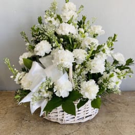 White floral arrangement in a wicker basket with a satin ribbon