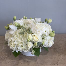 White floral arrangement in a low round vase with roses and hydrangeas