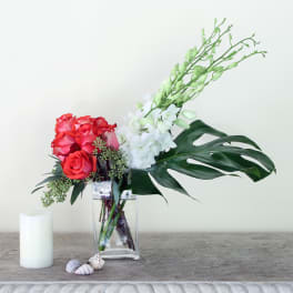 Red roses and white orchids in a clear vase with large tropical leaves