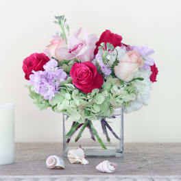 Bouquet of pink and white roses with lavender flowers in a square glass vase