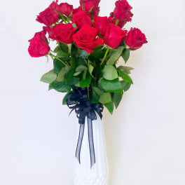 Bouquet of hot pink roses in a white vase with a dark ribbon