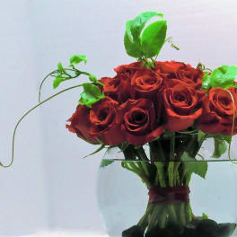Compact bouquet of red roses in a round glass bowl with looping green vines