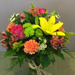 Mixed bouquet with yellow lilies, pink roses, and orange carnations in a glass vase