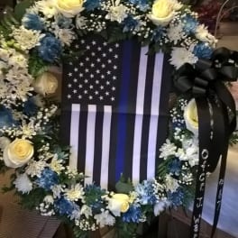 Floral wreath around a black-and-white flag display with yellow roses and blue flowers