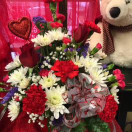 Red and white flower arrangement with a teddy bear and heart decorations