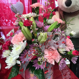 Mixed pink and white flower arrangement in a glass vase with a teddy bear