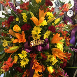 Large mixed bouquet with orange lilies, yellow daisies, and red flowers tied with a purple ribbon