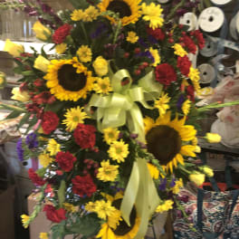 Large standing floral spray with sunflowers, red carnations, and yellow roses