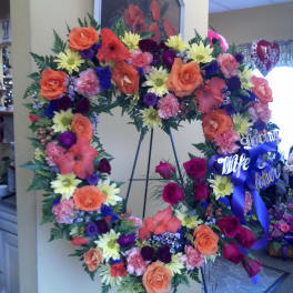 Large floral wreath on an easel with roses, daisies, and ribbon