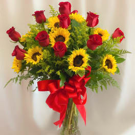 Bouquet of red roses and yellow sunflowers in a clear glass vase with a red ribbon