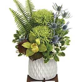 Green floral arrangement in a white textured pot on a wooden stand
