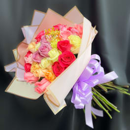 Bouquet of multicolored roses wrapped in pastel paper with a purple ribbon