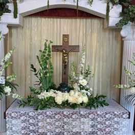 White floral funeral altar with tall arrangements and a crucifix
