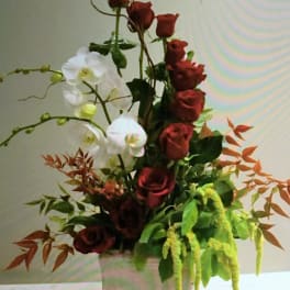 Tall arrangement of red roses and white orchids in a white vase