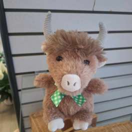 Small brown plush cow with curled horns and a green checkered bow displayed on a glass shelf.