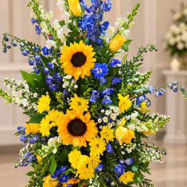Tall floral arrangement with sunflowers, yellow roses, and blue flowers