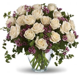 White roses and purple filler flowers in a clear glass vase