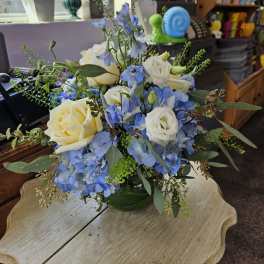 Low arrangement of white roses and blue flowers in a round green glass vase on a small table.