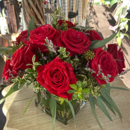 Red roses arranged in a clear square vase with mixed greenery