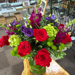 Bouquet of red roses, purple lisianthus, and green hydrangea in a glass vase