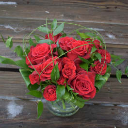 Red roses arranged in a clear glass vase with green foliage