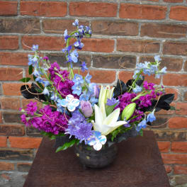 Mixed bouquet with white lilies, purple blooms, and blue flowers in a dark vase