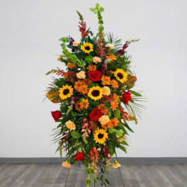 Tall standing floral spray with sunflowers, red roses, and orange blooms