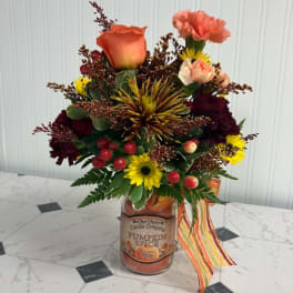 Mixed bouquet in a pumpkin spice candle jar with a striped ribbon
