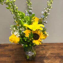 Yellow lilies, sunflowers, and roses in a glass vase with a Brewers logo