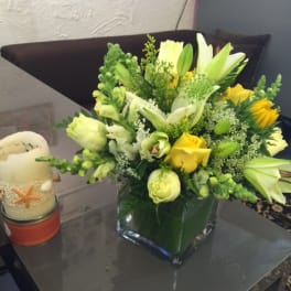 Yellow and white floral arrangement in a square glass vase