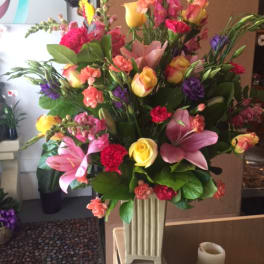 Tall mixed bouquet with pink lilies, yellow roses, and purple blooms in a vase