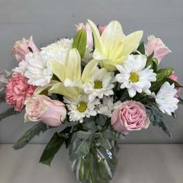 Pink roses, white daisies, and pale yellow lilies in a glass vase