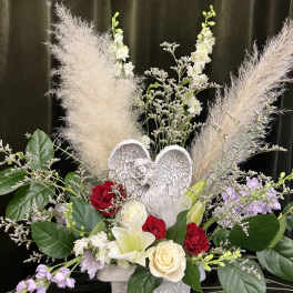 Mixed floral arrangement with roses, lilies, and an angel figurine in a white urn