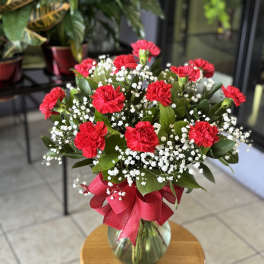 Red carnations and baby's breath in a glass vase with a red ribbon