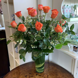 Orange roses arranged in a tall green vase with small white filler flowers.