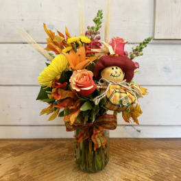 Fall bouquet in a glass vase with a small scarecrow decoration