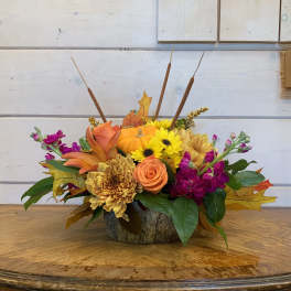 Autumn floral arrangement with sunflowers, roses, and a small pumpkin in a rustic container.