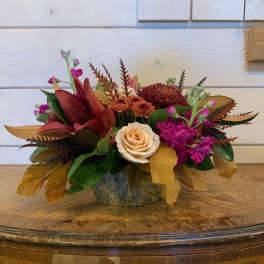 Low floral arrangement with roses, chrysanthemums, and magenta blooms in a rustic container