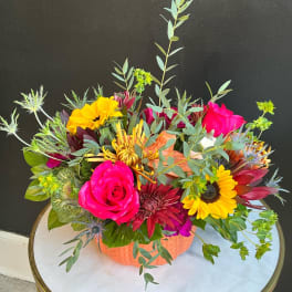 Bright mixed flower arrangement in an orange container with roses and sunflowers