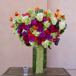 Bright mixed bouquet in a tall glass vase with pink, purple, and orange flowers.