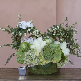 White and green floral arrangement in a moss-covered container