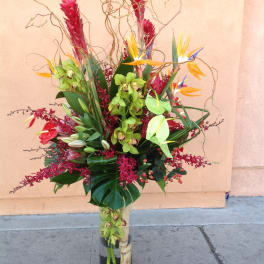 Tall tropical flower arrangement in a glass vase with red, green, and orange blooms