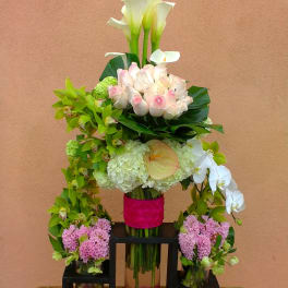 Tiered floral arrangement with white calla lilies, pink roses, and orchids in glass vases