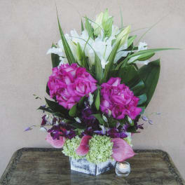 Tall floral arrangement with pink roses, white lilies, and pink calla lilies in a square vase.