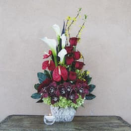 Tall floral arrangement with red roses, white calla lilies, and orchids in a white vase