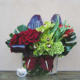 Red roses and green orchids arranged in a clear square vase